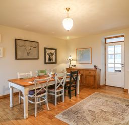 A dining room with a wooden table and mixed color chairs near a wooden sideboard and door at Ballintlea Ballintlea near Dungarvan County Waterford