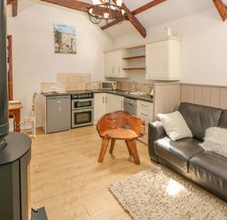 A rustic kitchen and living area with wooden beams wooden chair black leather sofa and wood stove at The Barn at Waunlippa Narberth