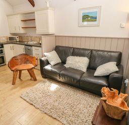 A living area with a black leather sofa and wooden chair next to a kitchen with white cabinets at The Barn at Waunlippa in Narberth