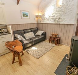 A living area with a black leather sofa three cushions a wooden chair a small rug and a wood-burning stove at The Barn at Waunlippa in Narberth