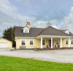 A yellow house with a gravel driveway and detached garage surrounded by grass at The Sanctuary in Killavullen near Mallow