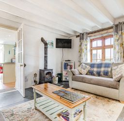 A living room with two sofas a coffee table a wood-burning stove a wall-mounted TV and a window with curtains at Victoria Cottage in St Newlyn East near Newquay