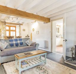 A living room with a sofa coffee table wood stove and dining area at Victoria Cottage St Newlyn East near Newquay