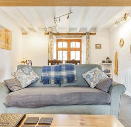 A living room with a sofa a coffee table paintings on the wall and a wooden window at Victoria Cottage in St Newlyn East near Newquay