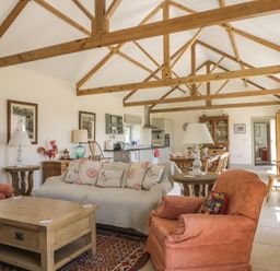 An open living room and kitchen with sofa armchairs wooden tables beams and dining area at Cow Byre in Malton