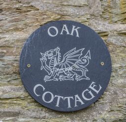 A round black sign with a dragon and the words Oak Cottage on a stone wall at Oak Cottage in Bryngwenith near Newcastle Emlyn