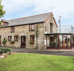 A stone cottage with glass conservatory and balcony overlooking a lawn at Oak Cottage in Bryngwenith near Newcastle Emlyn