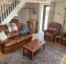 A living room with brown leather sofa and chairs a wooden coffee table and staircase at Oak Cottage in Bryngwenith near Newcastle Emlyn