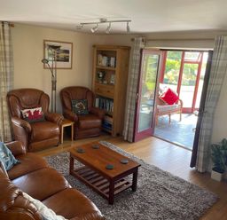 A living room with leather armchairs a wooden coffee table a bookshelf and a door leading to a sunroom with wicker furniture at Oak Cottage in Bryngwenith near Newcastle Emlyn