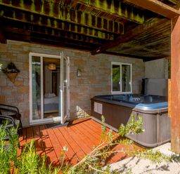 A patio with a hot tub two chairs and open doors leading to a bedroom at Brookside in Honicombe Manor near Gunnislake