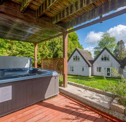 An outdoor covered wooden deck with a hot tub overlooking houses and green lawn at Brookside in Honicombe Manor near Gunnislake