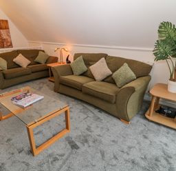 A living room with two sofas a glass coffee table side tables a large plant and a wall decoration at Brookside in Honicombe Manor near Gunnislake
