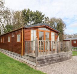 A wooden cabin with a small fenced porch on a grassy area at Broad Down in Berrow