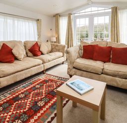 A living room with two beige sofas with red and beige cushions and a wooden table with a book in Broad Down Berrow