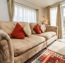 A beige patterned sofa with red and beige cushions in a living room with curtains and glass doors showing a garden at Broad Down in Berrow