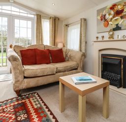 A living room with a sofa red cushions coffee table fireplace and glass doors at Broad Down in Berrow