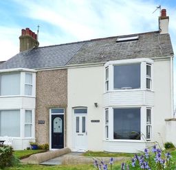 A semi detached house with two bay windows and a small garden with flowers at Sandy Bank in Rhosneigr