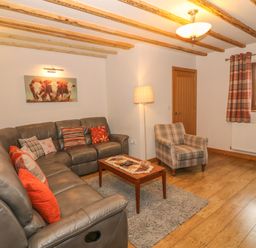 A living room with a leather sectional sofa with cushions a plaid armchair a wooden coffee table and a window with checked curtains at Caer Moel in Caernarfon
