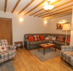 A living room with wooden floor beams plaid armchairs a gray sectional sofa and a wooden coffee table at Caer Moel in Caernarfon