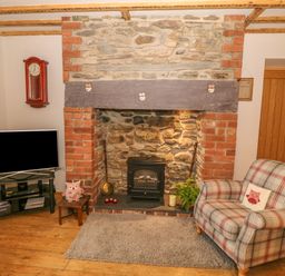 A sitting area with a plaid armchair a stone and brick fireplace a wall clock and a television at Caer Moel in Caernarfon