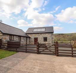 A stone barn with a gated driveway and solar panels on the roof at Beudy Bach Barn in Llanuwchllyn near Bala
