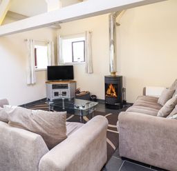 A living room with two sofas a glass coffee table a television and a wood burning stove at Beudy Bach Barn in Llanuwchllyn near Bala