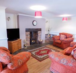 A living room with orange patterned sofas a television on a wooden stand a brick fireplace and a red patterned rug at Arfryn in Bethesda
