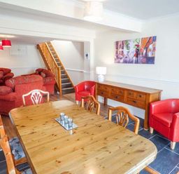A dining room with wooden table and chairs next to a sideboard and red armchairs with a staircase and red sofas in the background at Arfryn in Bethesda