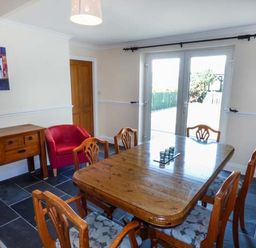 A dining room with a wooden table and chairs a red armchair a wooden sideboard and glass doors at Arfryn in Bethesda