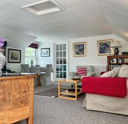 A living room with a beige sofa and armchair a wooden coffee table and a wooden sideboard with a flower vase at The Boat House in Golant near Tywardreath