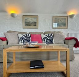 A sofa with cushions and red throws with a wooden coffee table in front of it at The Boat House in Golant near Tywardreath