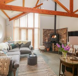 A living room with a grey sectional sofa wood burner and a glass table with flowers at The Wagon House in Tresmeer near Launceston
