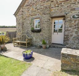 A stone cottage entrance with a wooden bench and potted plants at Dovecote in Gorran Haven