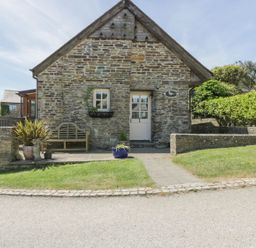 A stone cottage with a white door and window a wooden bench and potted plants outside at Dovecote in Gorran Haven