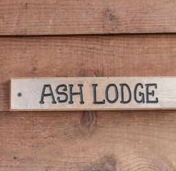 A wooden sign with ASH LODGE mounted on a wooden wall at The Ash Lodge near Lyme Regis