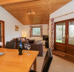 A living room and dining area with a wooden ceiling and double doors leading outside at The Ash Lodge near Lyme Regis