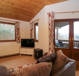 A living room with sofas a television and large windows overlooking a balcony at The Ash Lodge near Lyme Regis
