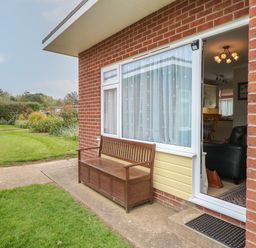 A wooden bench outside a brick house with a glass door open to a living area at En-Casa in Mundesley