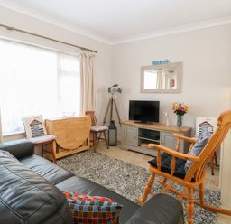 A living room with a black leather sofa wooden rocking chair TV on a stand and a small dining table at En-Casa in Mundesley