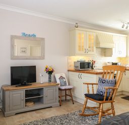 A living room with a wooden rocking chair and a television on a cabinet next to a kitchen at En-Casa in Mundesley