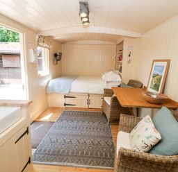 A small room with a bed a wooden table and wicker chairs a sink and a rug on the floor at Shepherd's Hut in Castleton Peak District