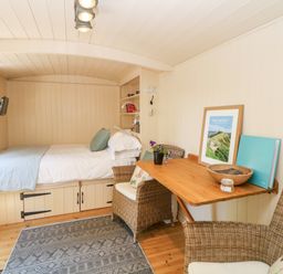 A small room with a bed under a window a wooden table with two wicker chairs and framed artwork at Shepherd's Hut in Castleton Peak District