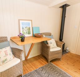 A small sitting area with two wicker chairs and a wooden table against a paneled wall at Shepherd's Hut in Castleton Peak District