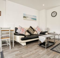 A living room with a black and white sofa and pillows a coffee table a dining table with chairs a wall clock and a painting at Plas Bach in Aberffraw