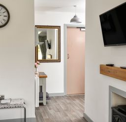 A hallway with a clock on the wall a bench a mirror a table with flowers a door a hanging light and a mounted television at Plas Bach in Aberffraw