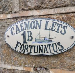 A sign stating CAEMON LETS 1B FORTUNATUS on a stone wall in Whitby