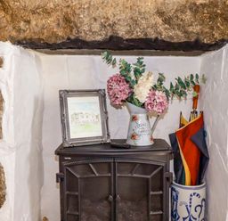 A living room with a wood stove and flowers on a shelf at Longview Cottage Penwithick neat St Austell