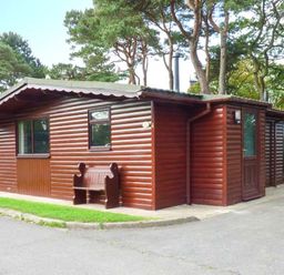 A brown wooden cabin with a bench outside surrounded by trees at Snowdrop in Saltburn-by-the-Sea