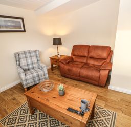 A living room with a brown sofa a plaid armchair wooden coffee table with decorations and a side table with a lamp at Snowdrop in Saltburn-by-the-Sea