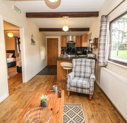 A living area with a plaid armchair wooden coffee table and kitchen in the background at Snowdrop in Saltburn-by-the-Sea